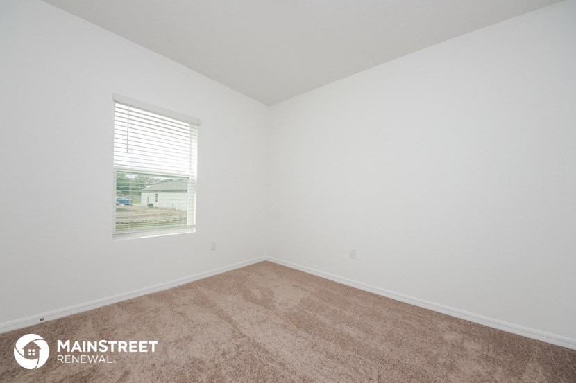 the living room of a small white house with carpet and a window