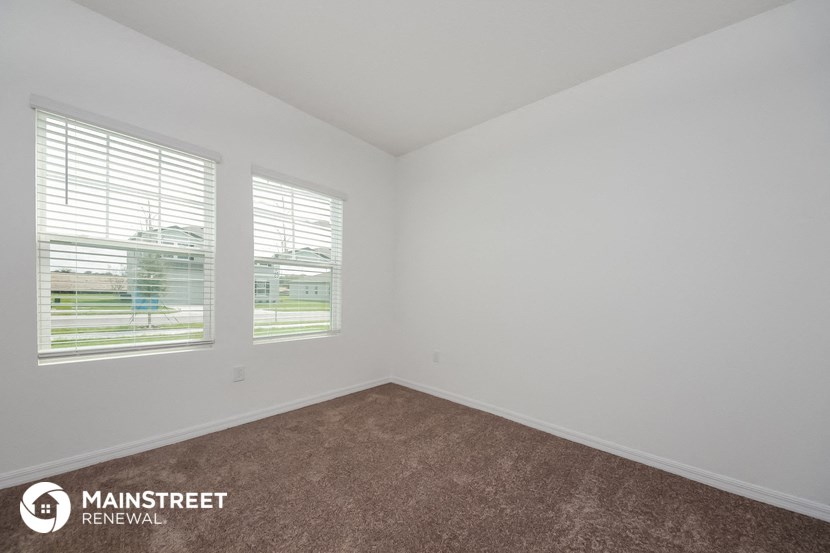 the living room of an apartment with carpet and three windows