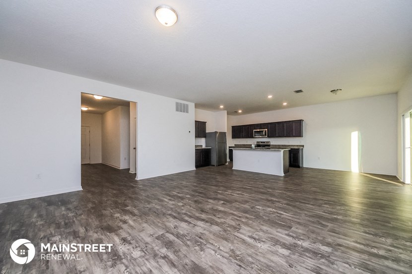 the living room and kitchen of an apartment with white walls and wood flooring