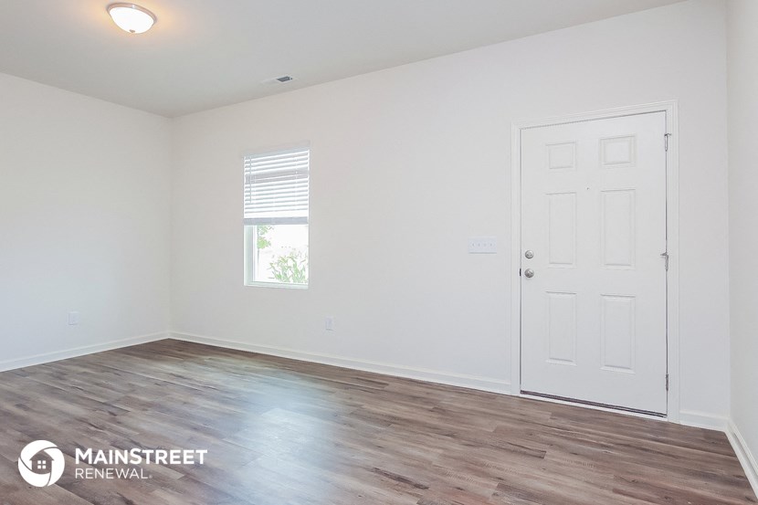 the living room of a small white house with wood floors and a white door
