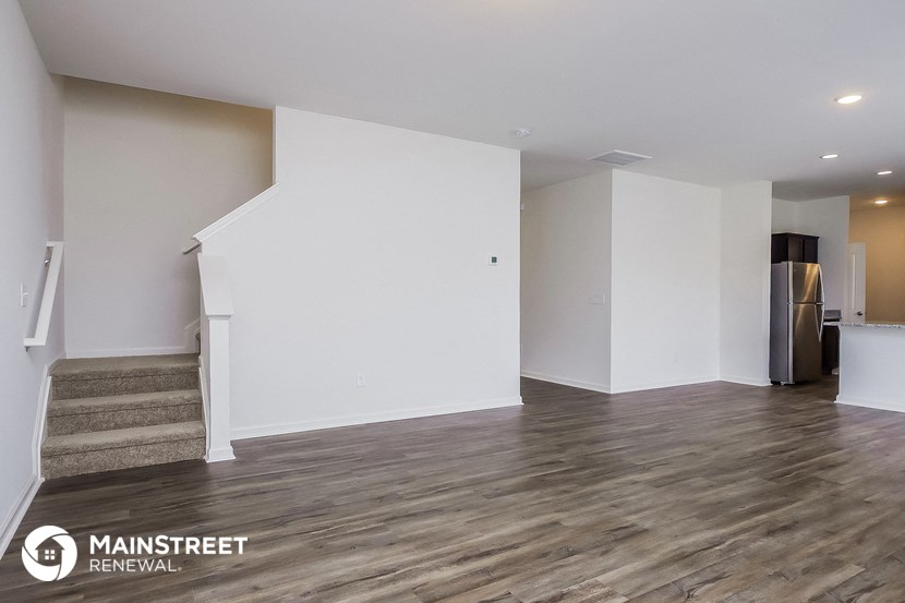 an empty living room with white walls and a stainless steel refrigerator