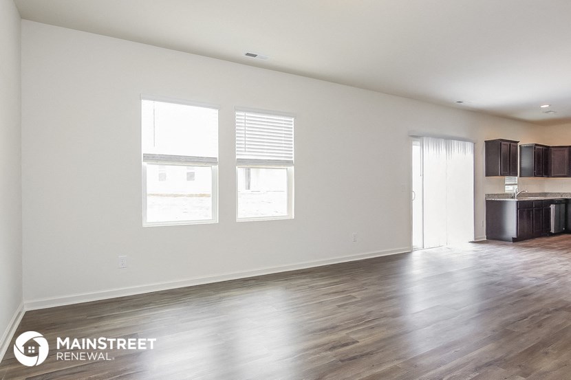 the living room and kitchen of an apartment with white walls and wood floors