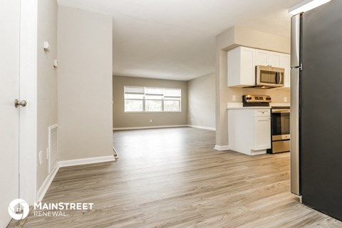 the kitchen and living room of an apartment with wood flooring and white cabinets