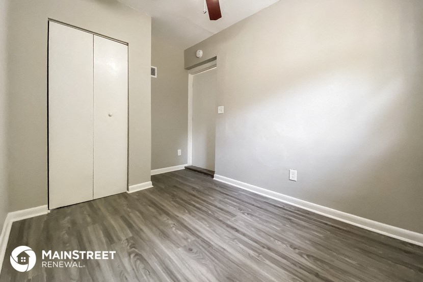 a bedroom with white walls and wood flooring and a closet