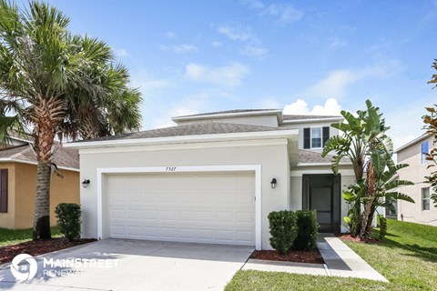 a white house with a garage door and palm trees