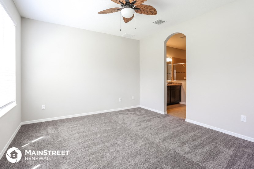 the spacious living room with carpeted flooring and a ceiling fan