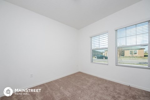 the living room of an apartment with carpet and two windows