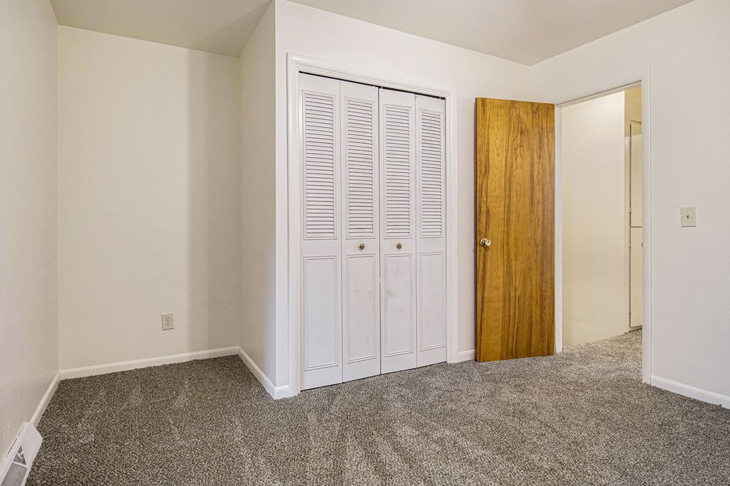 a bedroom with white doors and carpeting and a door to a closet