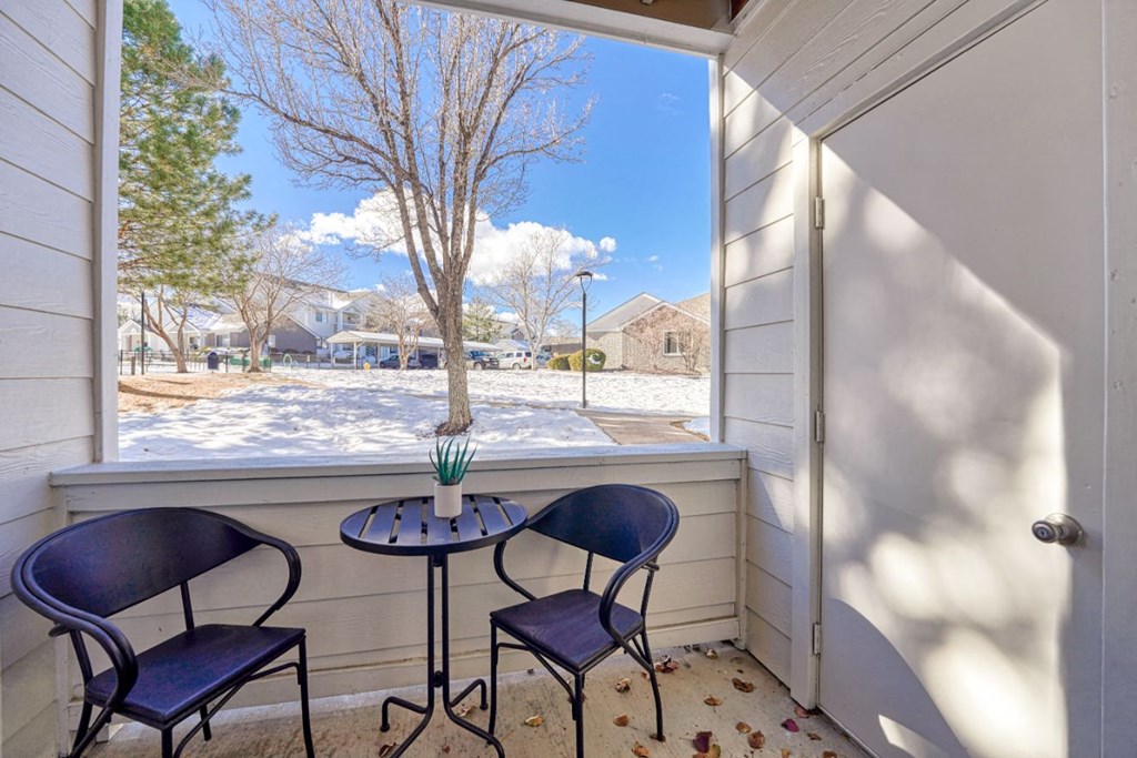 a small porch with two chairs and a table and a window