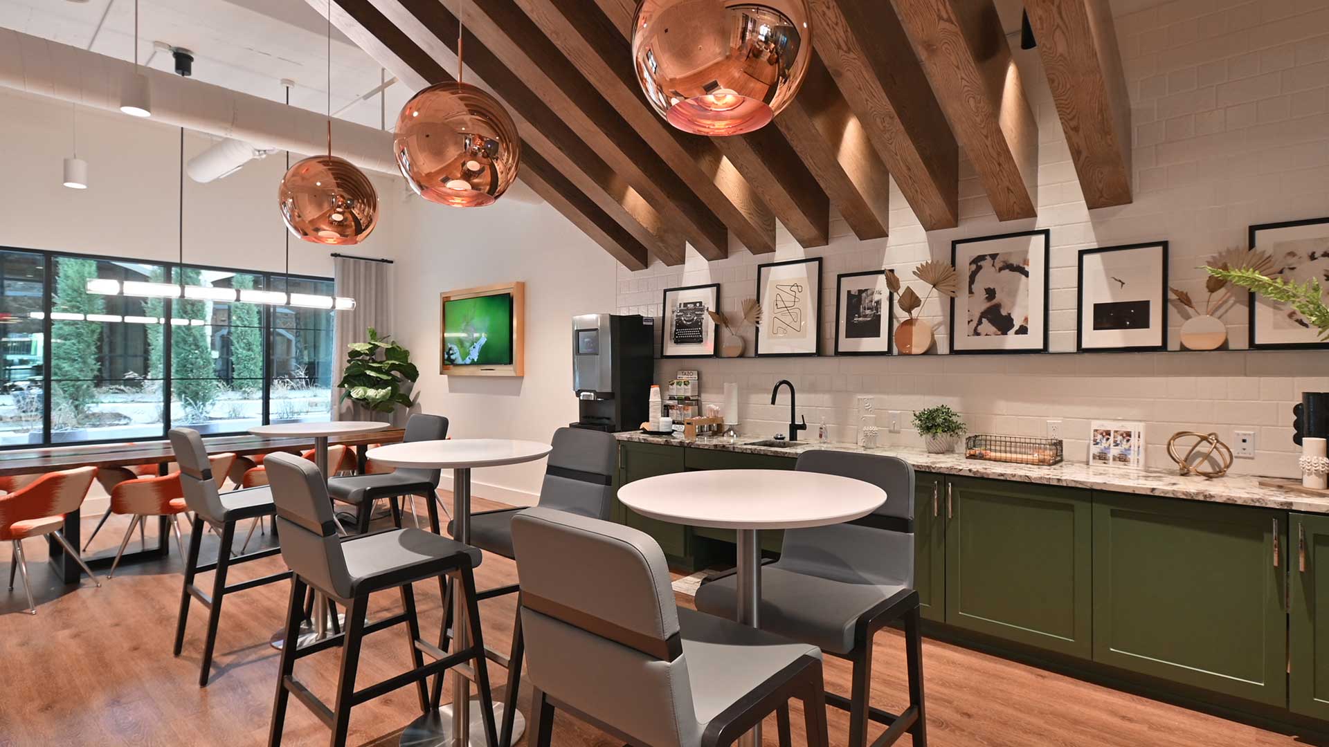 High top café tables site in front of a full coffee bar along the back wall. Large copper light fixtures hang from the ceiling.