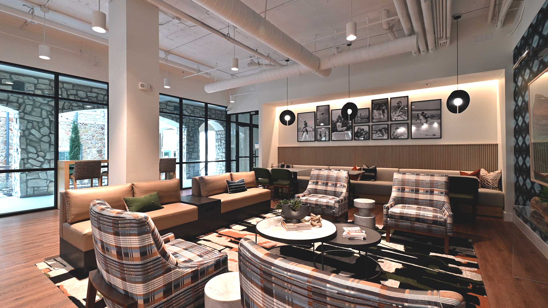 Several lounge chairs and couches sit in a square with additional bench seating behind along the wall. The the right are windows showing the walkway outside.