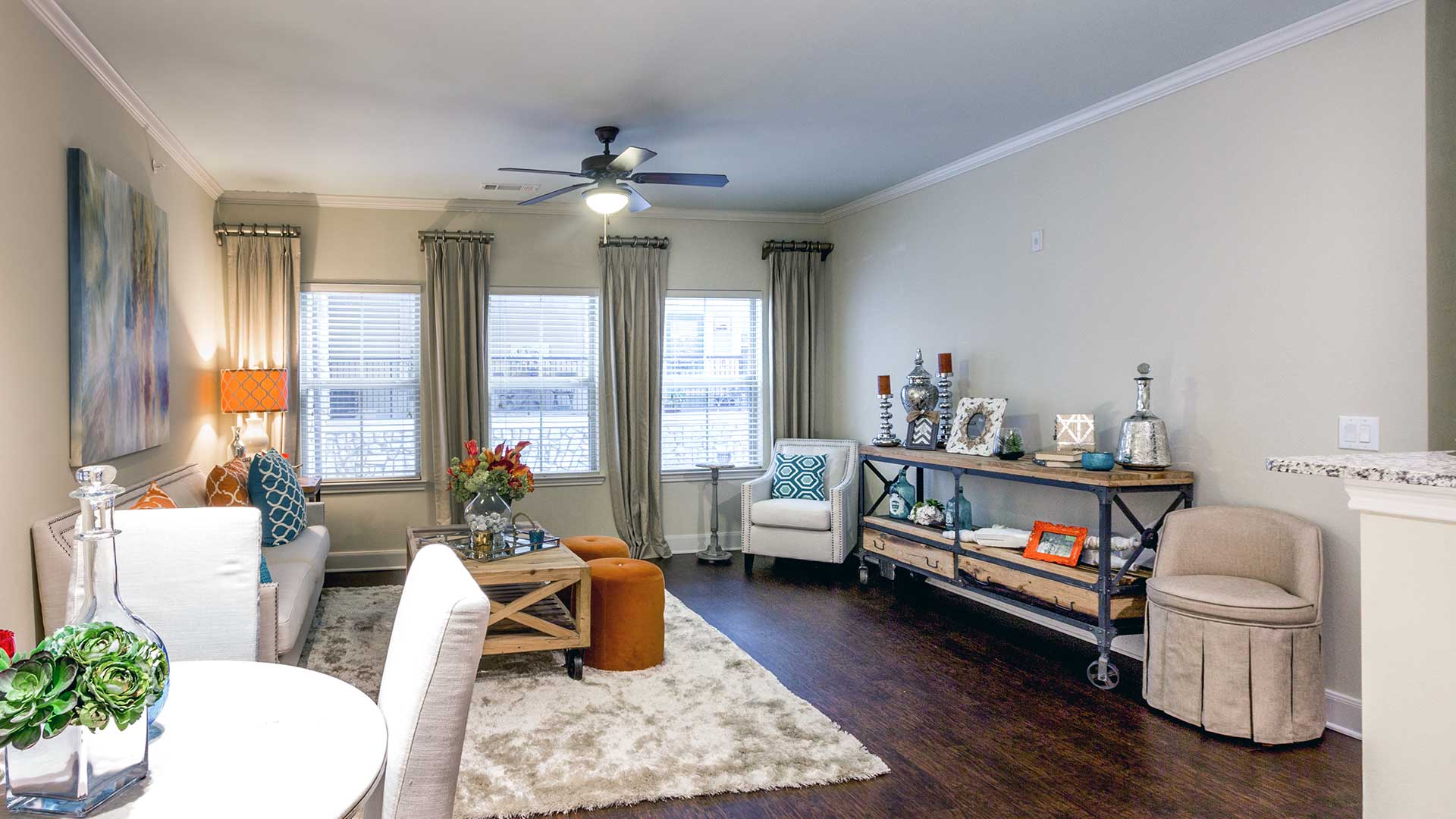 A living room in a residence at Bell Tower Flats. A small dining set is on the left with a couch and table further back. Windows line the back wall.