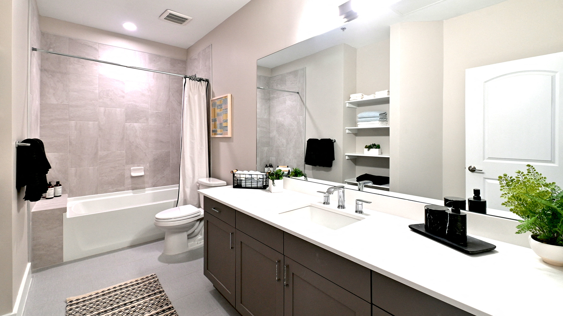 Looking at bathtub in a residence at Bell tower Flats, the shower curtain is drawn to the right. Along the right is the vanity and wall-mounted mirror.