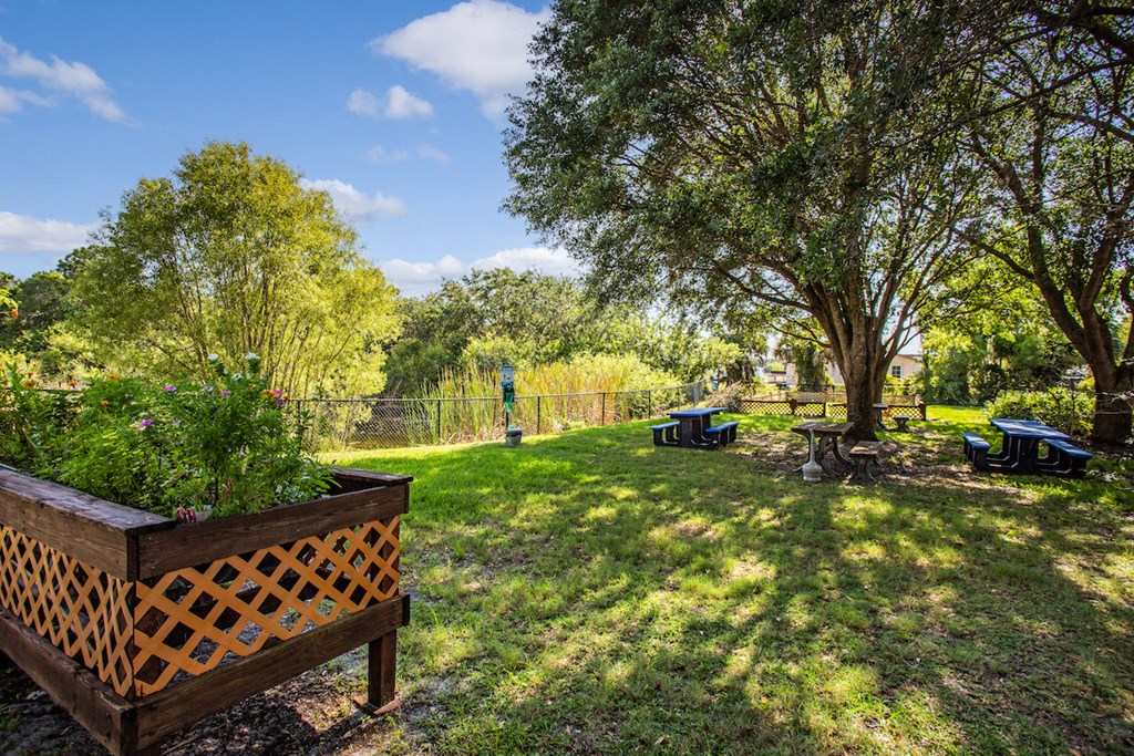 lush landscaping with garden boxes, mature trees, and picnic tables