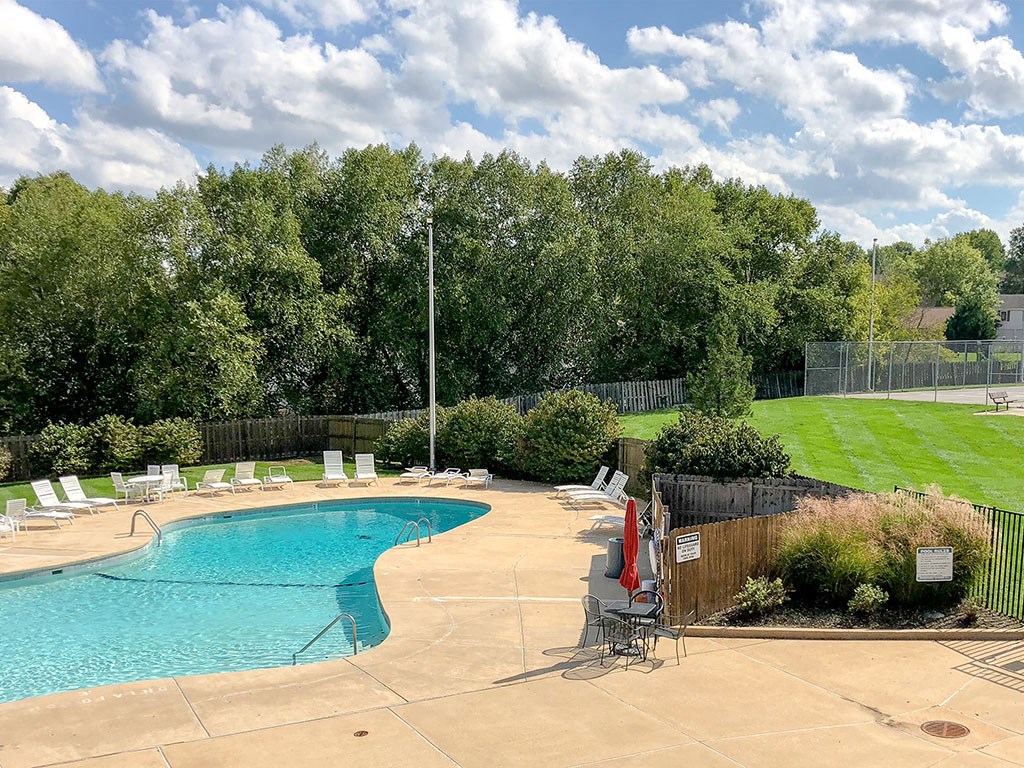 a swimming pool with chairs around it next to a lawn