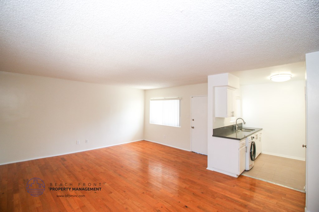 an empty kitchen and living room with wood flooring and white walls
