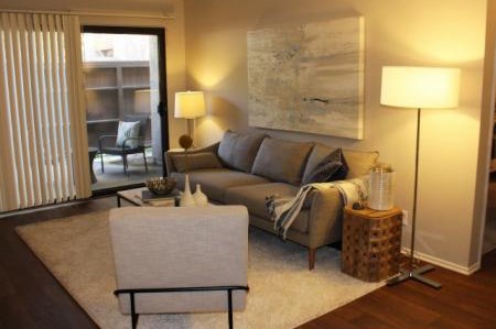 A living room with a grey couch, a white chair, and a large painting on the wall.