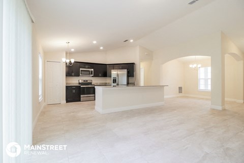 an open kitchen and living room with black cabinets and a white counter top