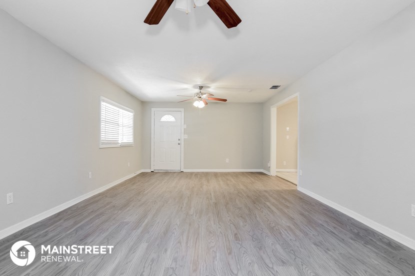 the spacious living room with wood flooring and ceiling fan