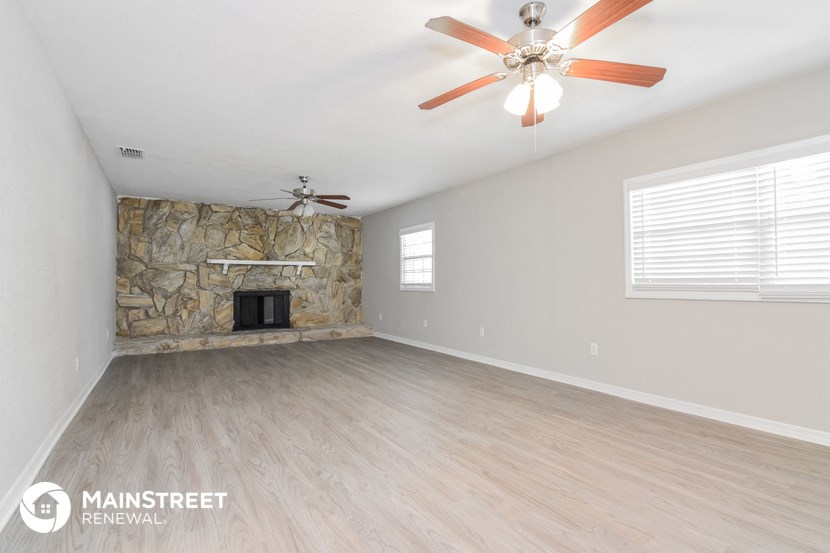 a living room with a stone fireplace and a ceiling fan