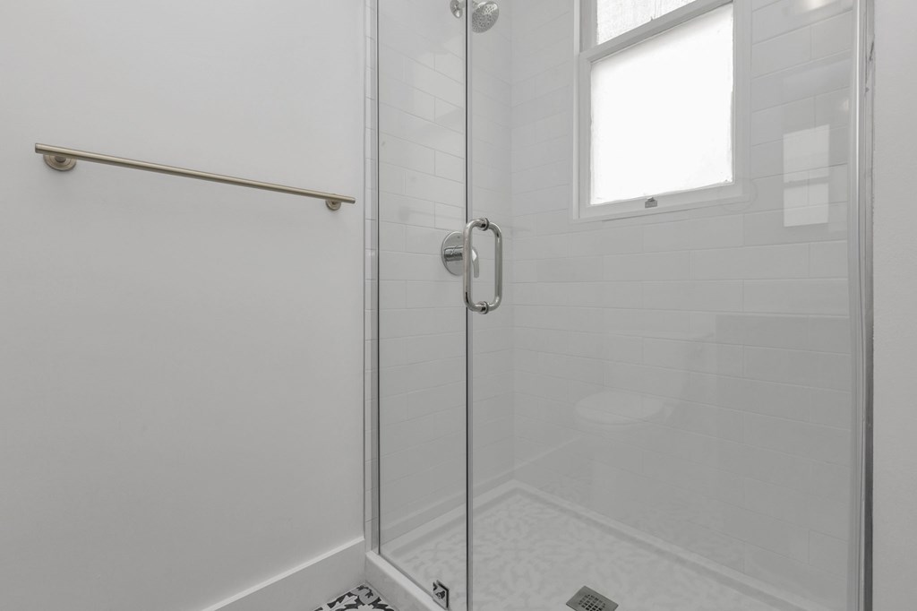 A white bathroom with a glass shower door and a window.
