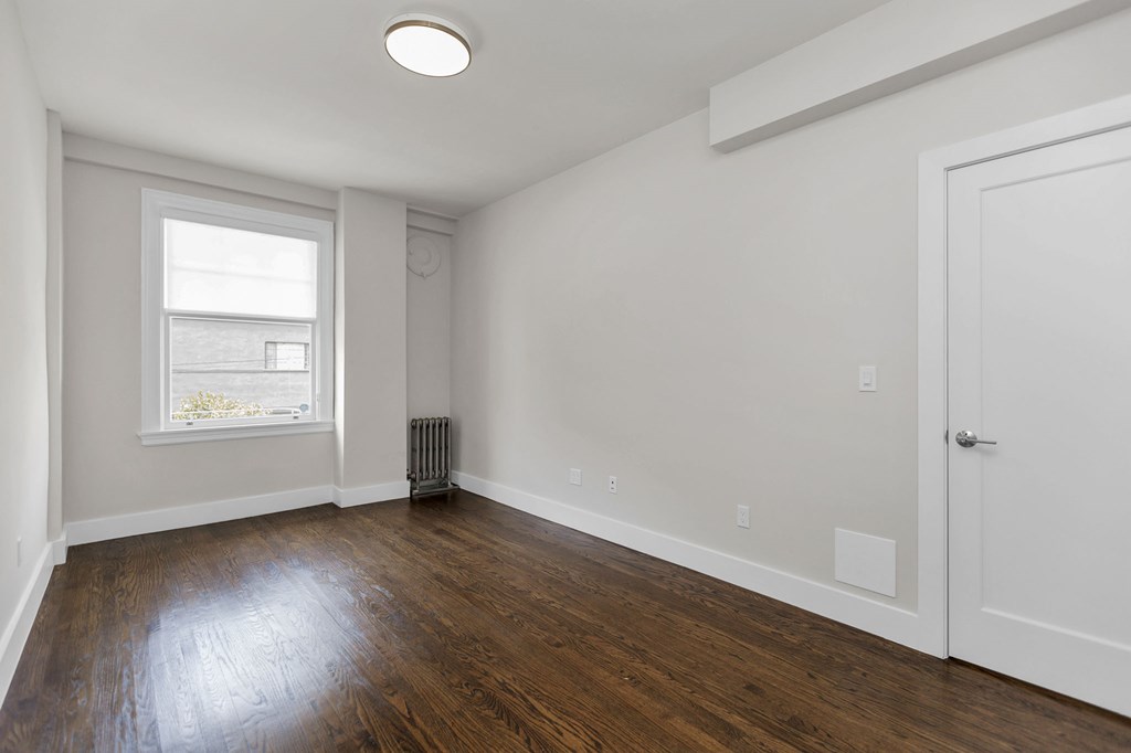 A room with a white door, a window, and a radiator.