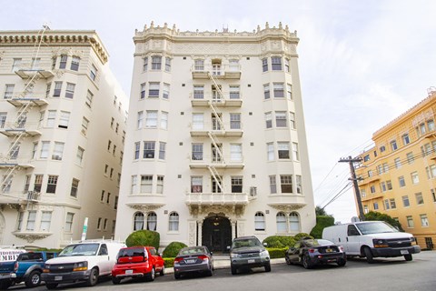 A row of cars are parked in front of a white building.