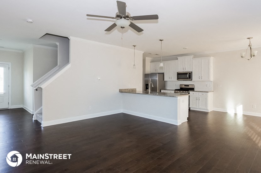an empty living room with a kitchen and a ceiling fan