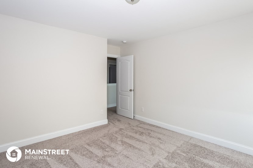 the living room of an apartment with white walls and carpet