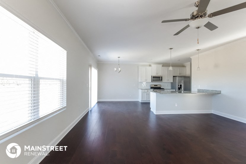 an empty living room with a kitchen and a ceiling fan