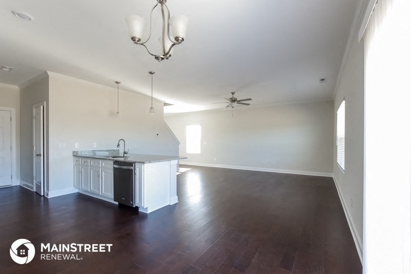 an empty living room with a kitchen and a ceiling fan
