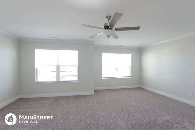 an empty room with a ceiling fan and two windows