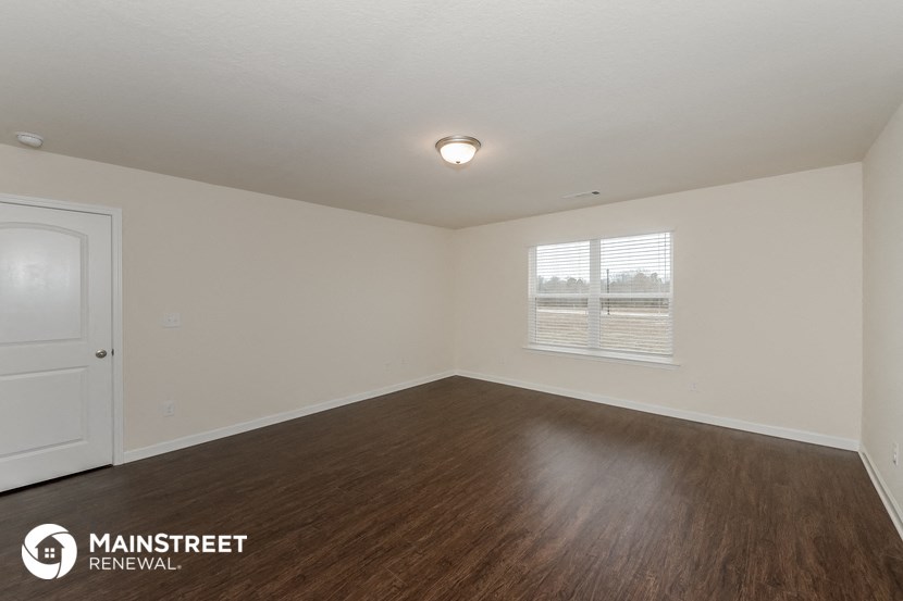 the spacious living room with wood flooring and a window