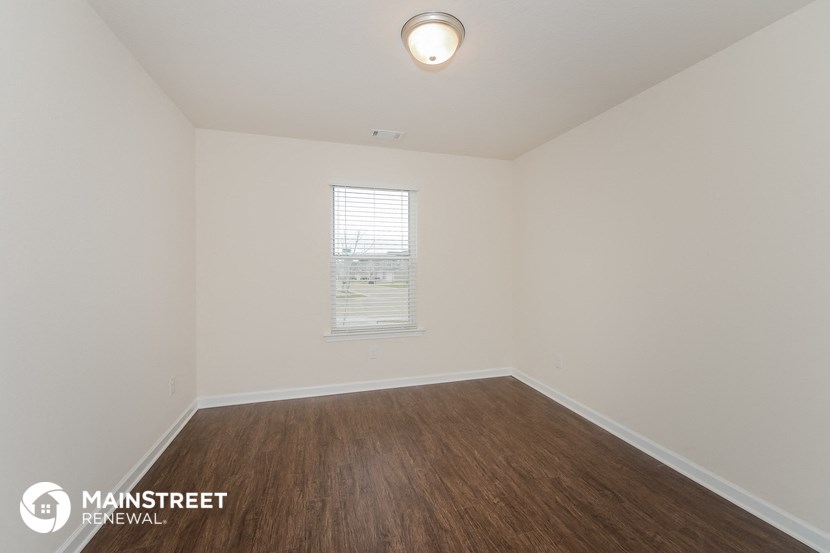 a bedroom with white walls and wood flooring and a window