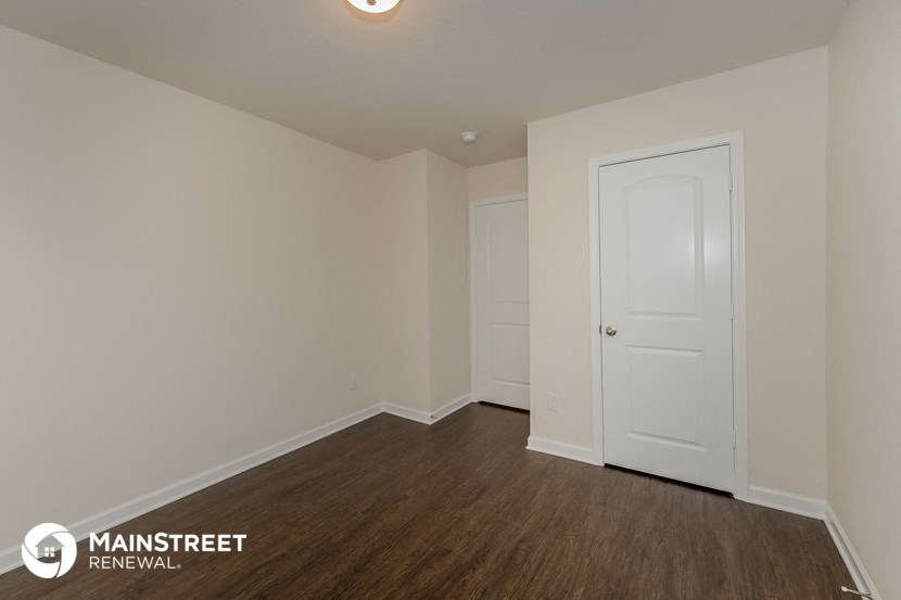 a bedroom with white walls and wood flooring and a white door