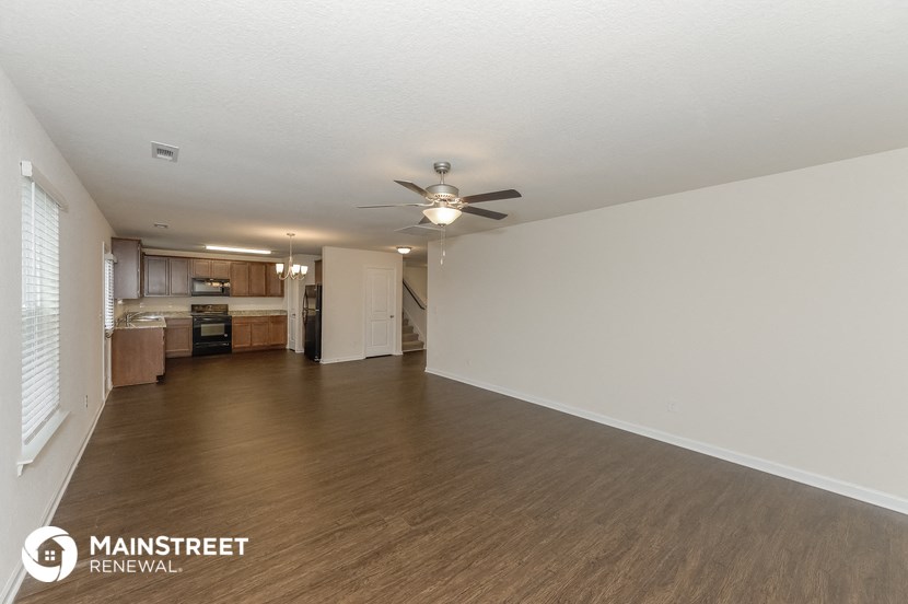 the living room and kitchen of an apartment with wood flooring and a ceiling fan