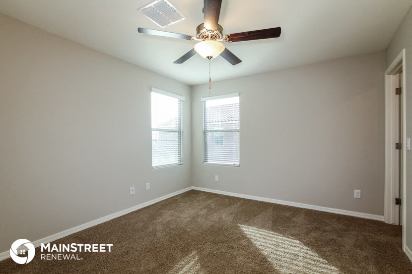 the spacious living room with ceiling fan and two windows