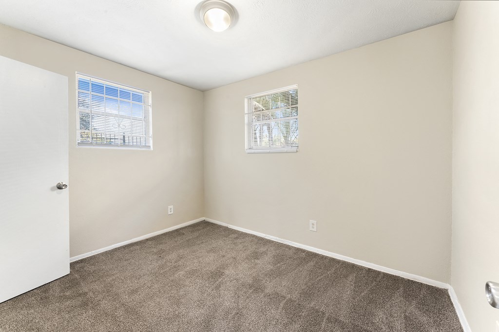 an empty room with carpet and two windows