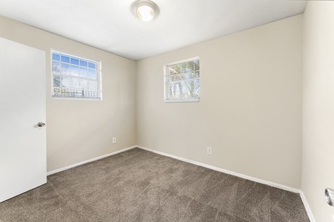 an empty room with carpet and two windows