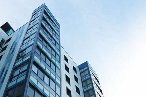 A tall building with many windows is seen against a blue sky.