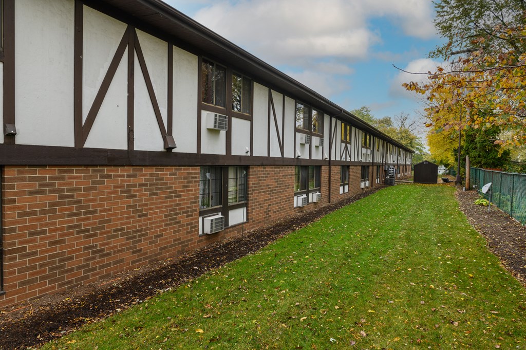 the side of a building with a green lawn and a brick wall