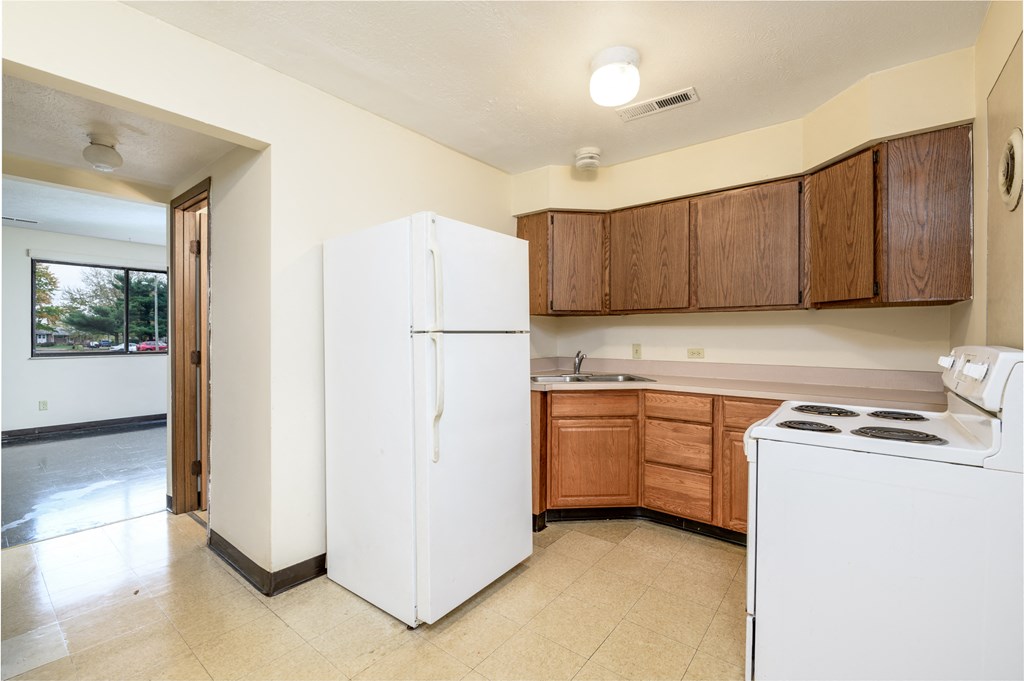an empty kitchen with white appliances and wooden cabinets