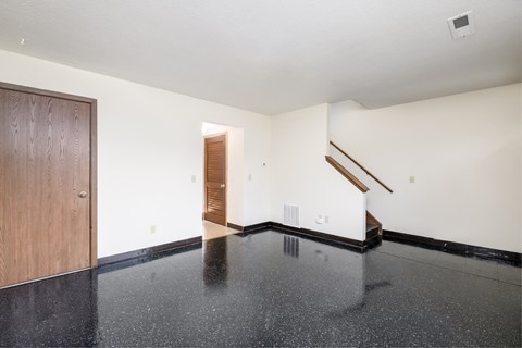 an empty living room with white walls and black flooring and a wooden door