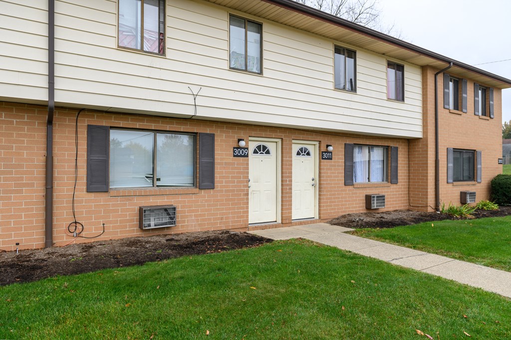 the front of a brick building with two white doors and a sidewalk