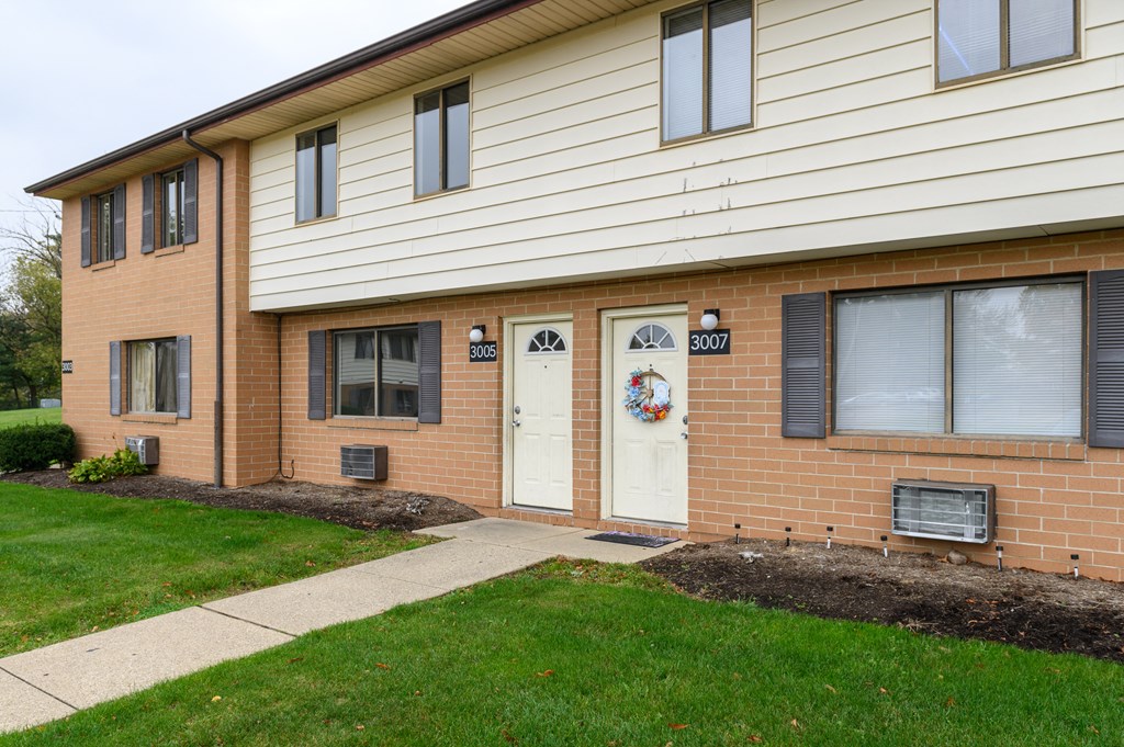 the front of a brick building with two white doors and a sidewalk