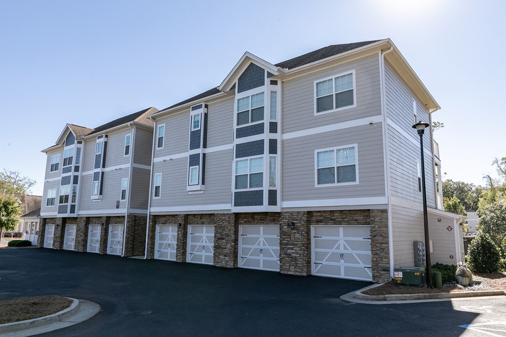 an apartment building with tan and white siding and white garage doors