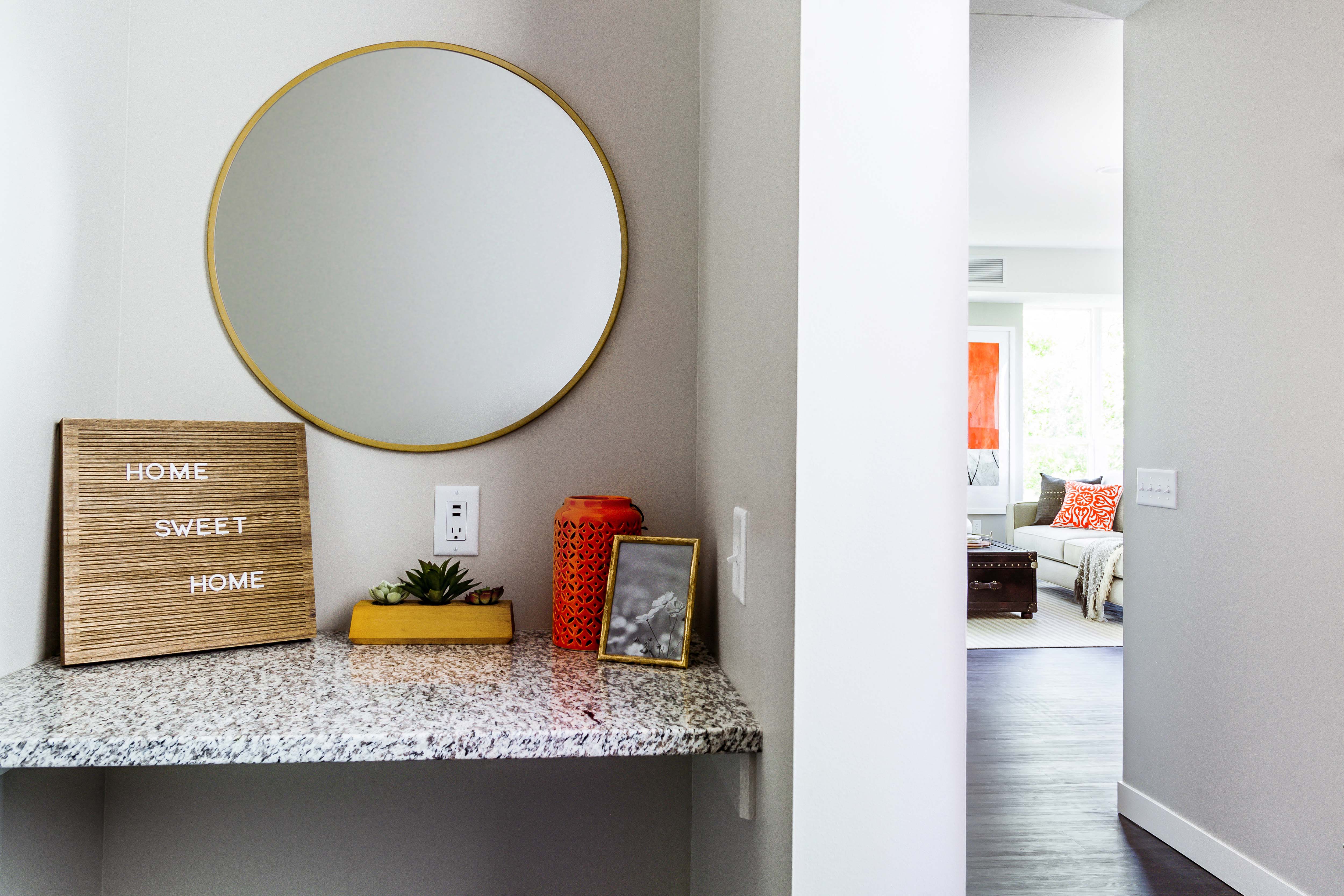 Entrance to a modern apartment: A sleek hallway vanity with a granite countertop welcomes guests, seamlessly transitioning into the well-lit living room flooded with natural light.