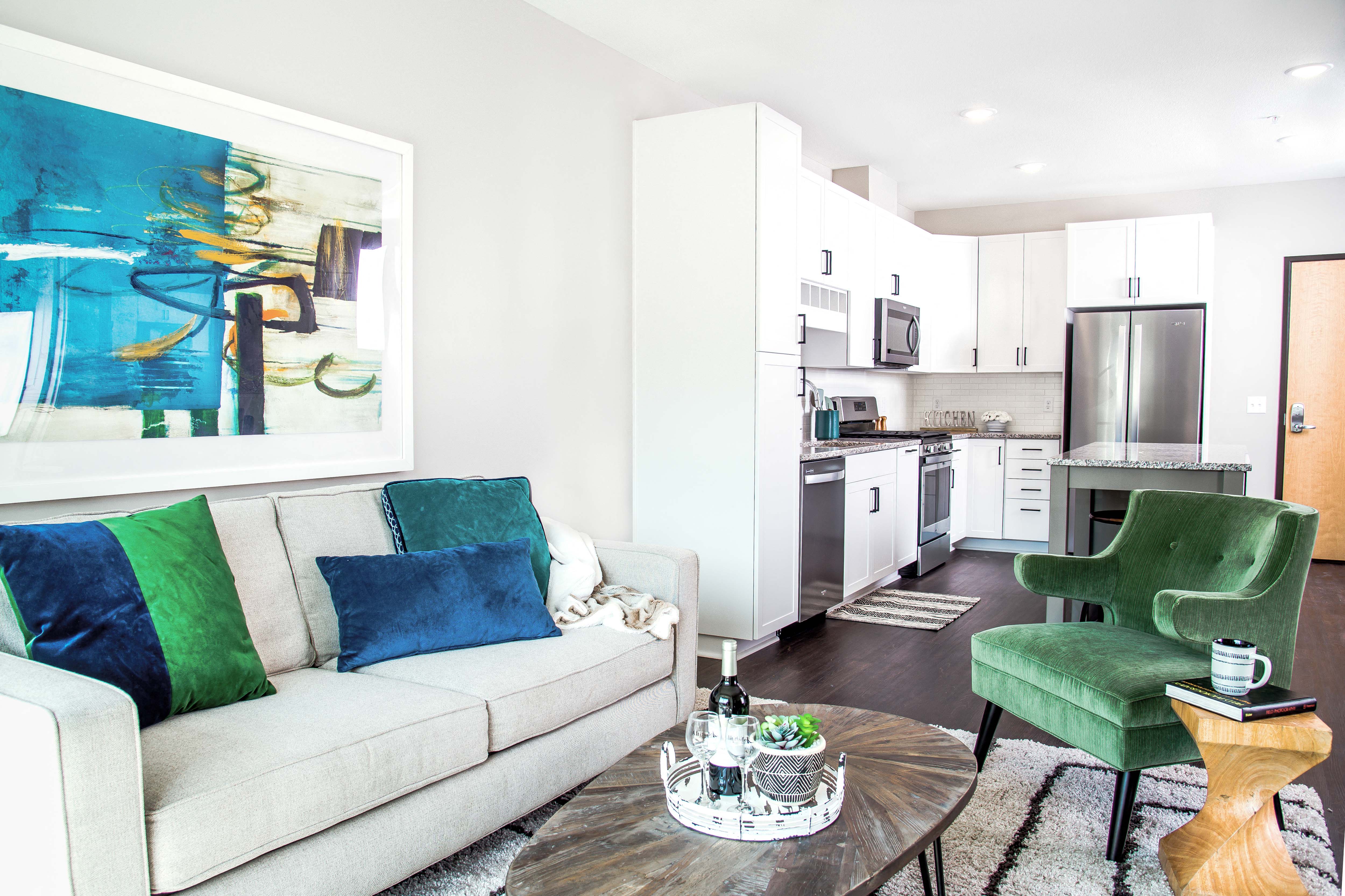 View from the living room capturing the warm and inviting ambiance, with stylish furniture and decor in the foreground. Beyond, the open kitchen is visible, adorned with modern appliances and a sleek design.