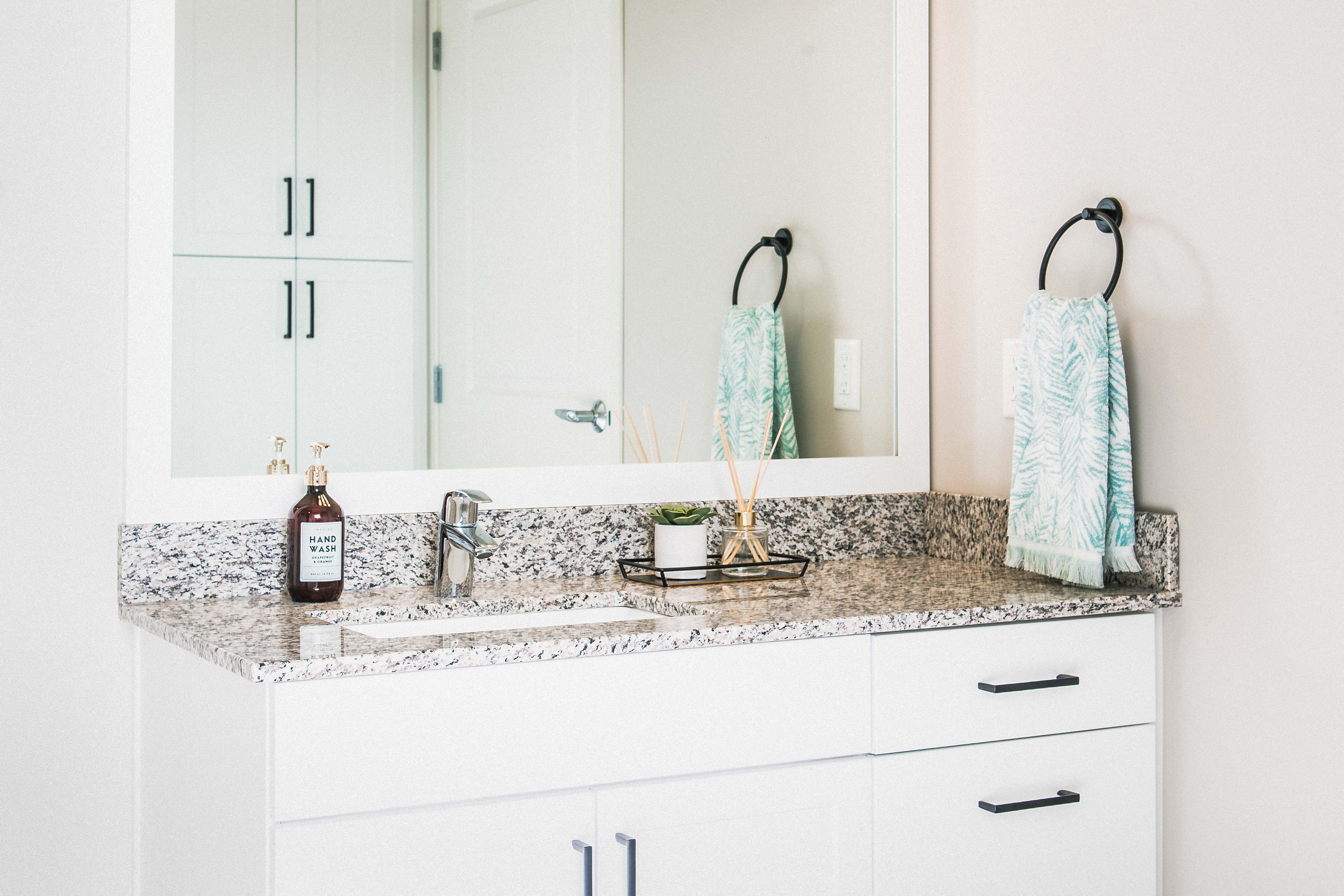 Inviting bathroom with elegant granite countertops, resilient stain-resistant plank flooring, and a modern shower.