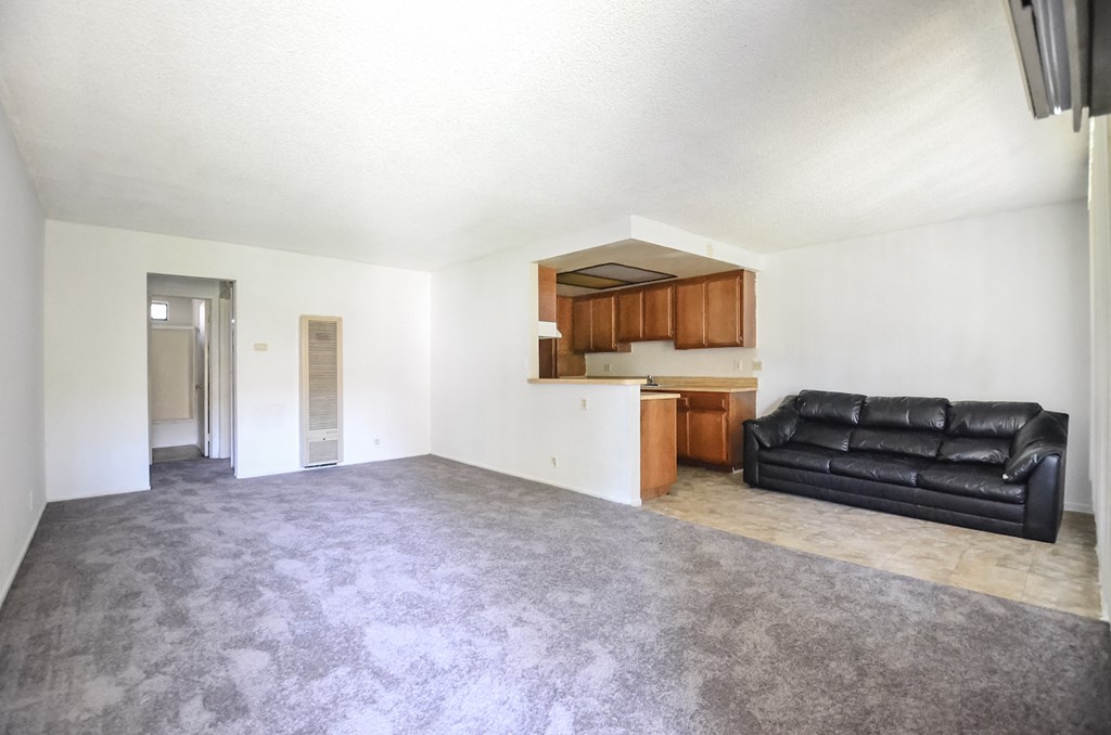 an empty living room with a black couch and a kitchen